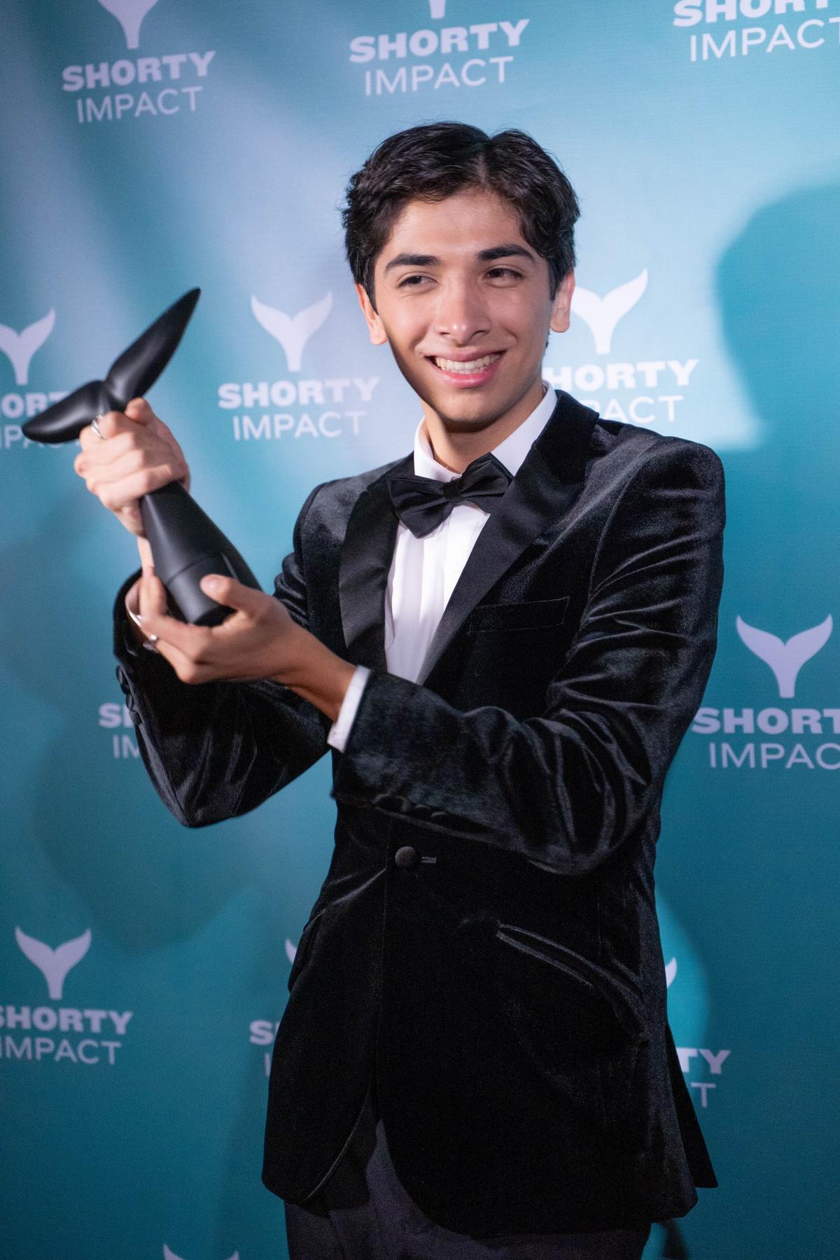 Joseph holding a Shorty Impact Award trophy in front of the Shorty Impact backdrop