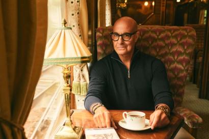 Stanley Tucci, wearing N.Peal knitwear, sits in a train carriage
