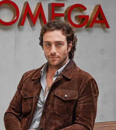 Aaron Taylor-Johnson stands in front of Omega sign at the watchmaker's Swiss headquarters