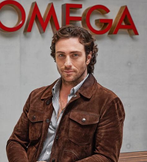Aaron Taylor-Johnson stands in front of Omega sign at the watchmaker's Swiss headquarters