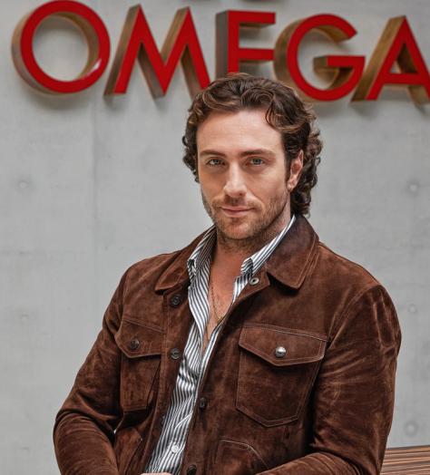 Aaron Taylor-Johnson stands in front of Omega sign at the watchmaker's Swiss headquarters