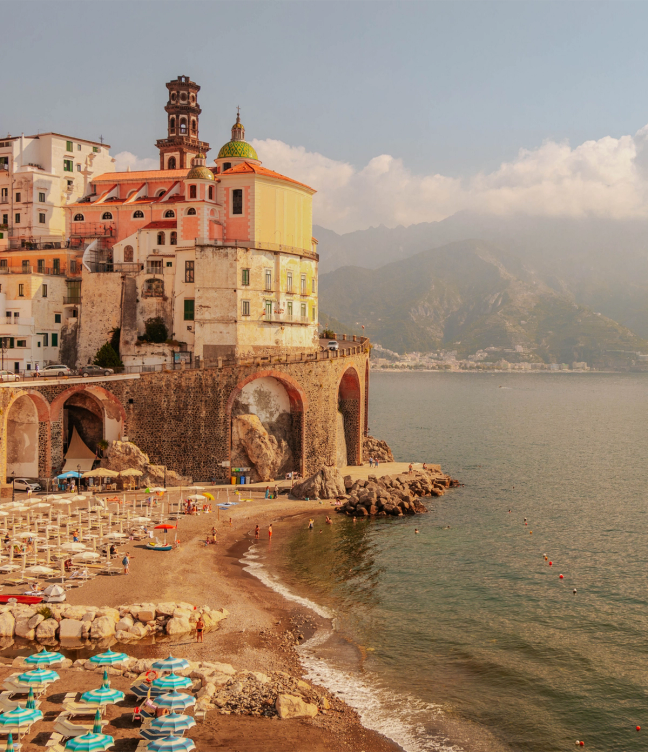 Beach full of umbrellas and sun loungers, with coastal road and buildings on the Amalfi Coast, Italy