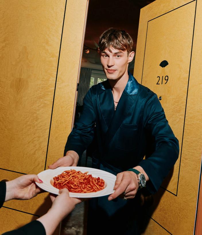 Model Kit Butler in a navy dressing gown holding a plate of spaghetti