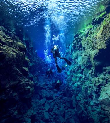 scuba diver swims underwater between rock crevices