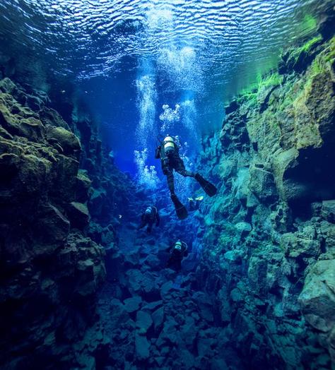 scuba diver swims underwater between rock crevices