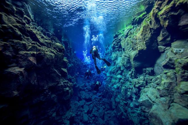 scuba diver swims underwater between rock crevices