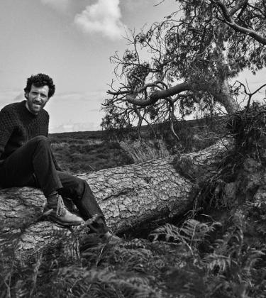 Man in thick Aubin jumper sat on a fallen tree