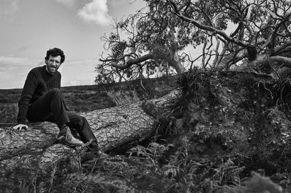 Man in thick Aubin jumper sat on a fallen tree