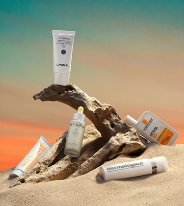 Four SPF bottles on sand and a branch, with a sunset background