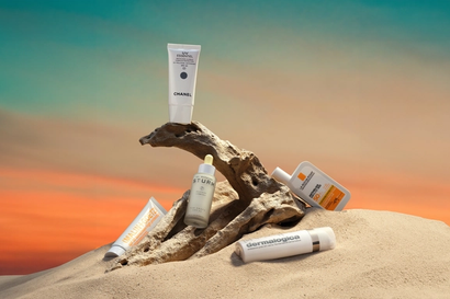 Four SPF bottles on sand and a branch, with a sunset background
