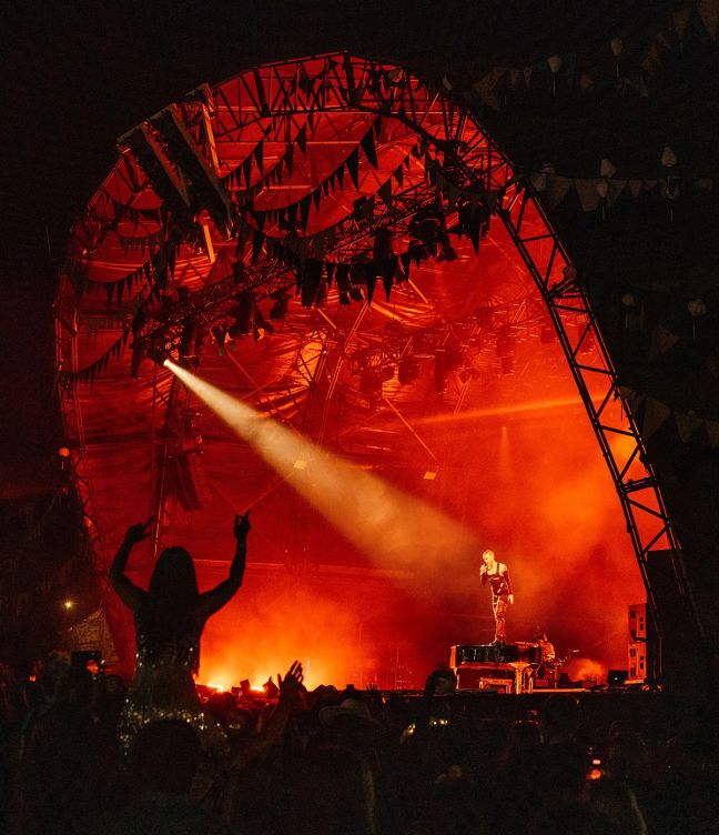 A red light filled Wilderness Festival Main Stage, with the silhouette of a girl sat on someone's shoulders