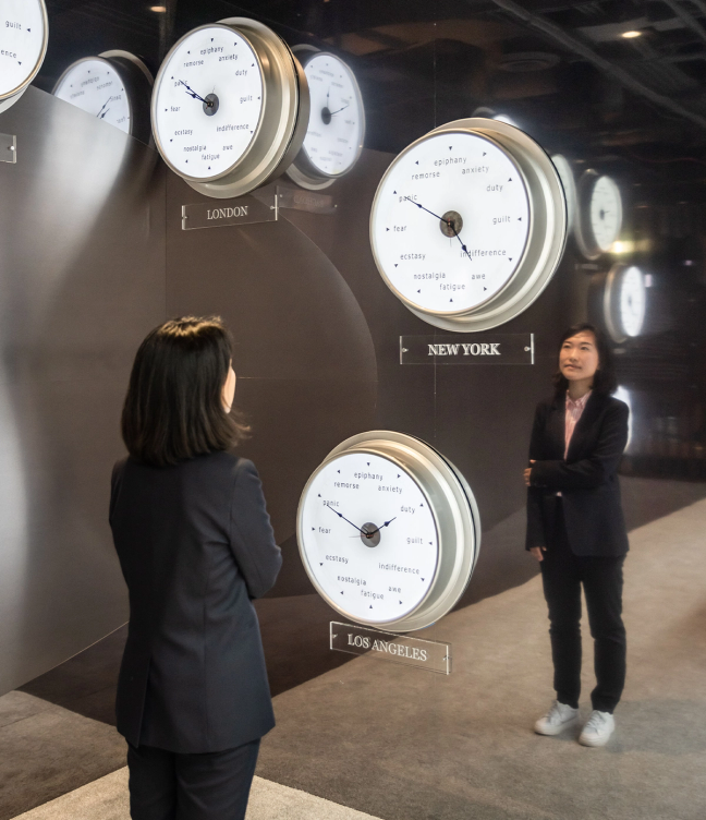 Curator Somi Sim standing in front of a wall of clocks