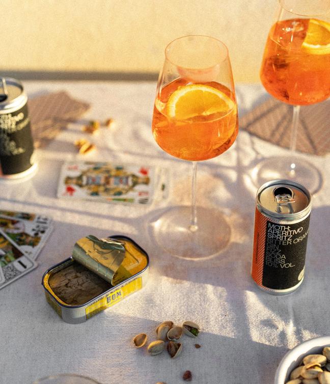 MOTH cans on a table at a party next to a glass on Aperitivo spritz
