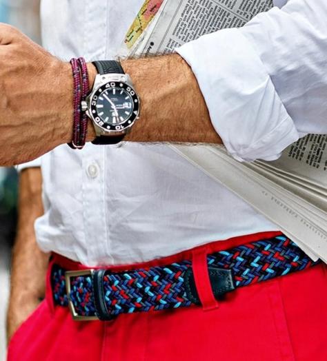 man holds iphone and wall street journal whilst wearing red chinos and anderson's multi coloured woven elasticated belt
