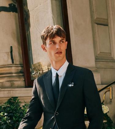 Model Kit Butler in a black suit walking out of a hotel lobby