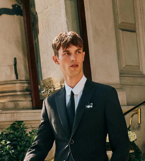 Model Kit Butler in a black suit walking out of a hotel lobby