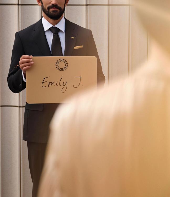 Driver in suit holding up a Wheely chauffeur name board for Emily J.