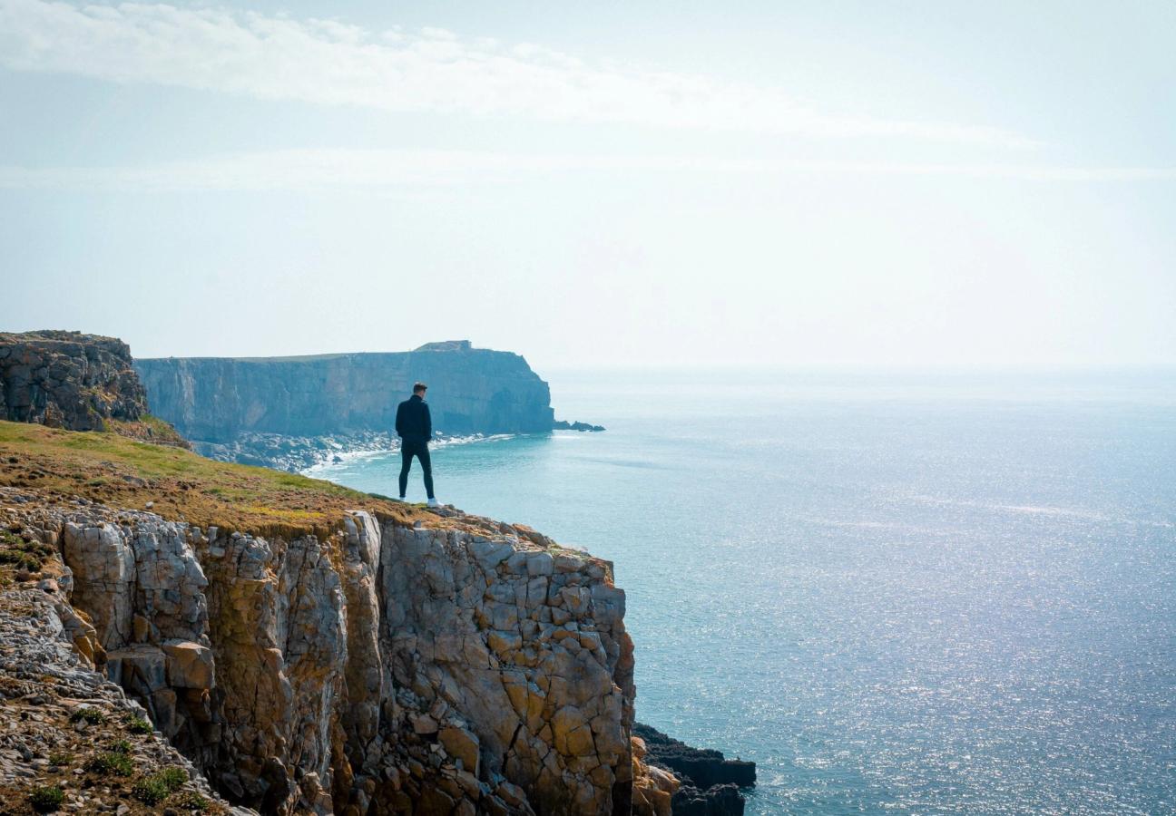 man looks over cliffs while coasteering