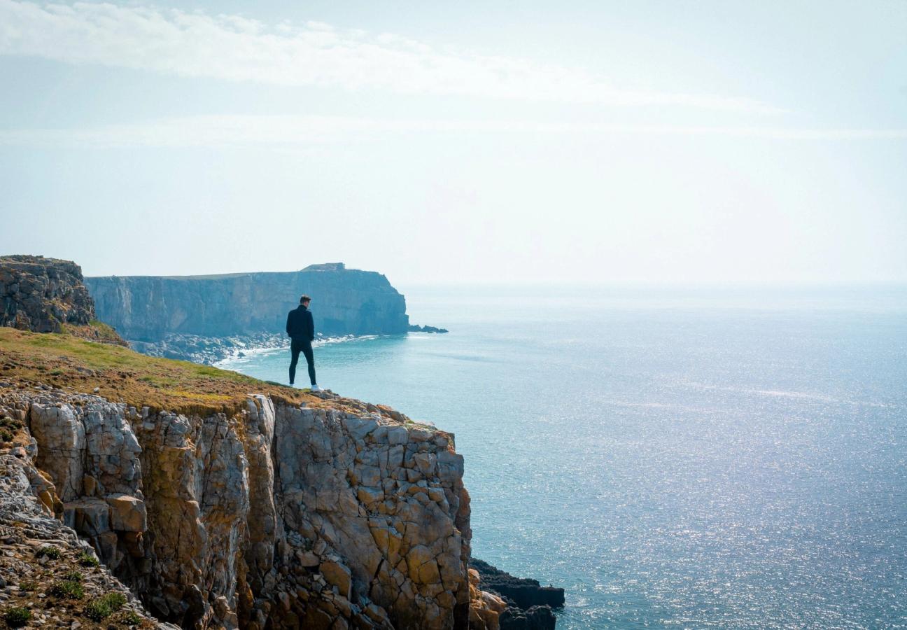 man looks over cliffs while coasteering
