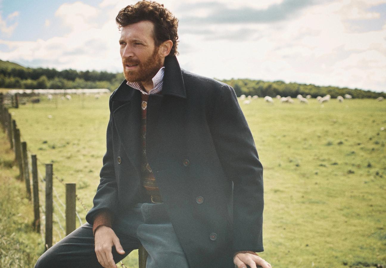 Man in navy Aubin jacket overlooking fields of sheep