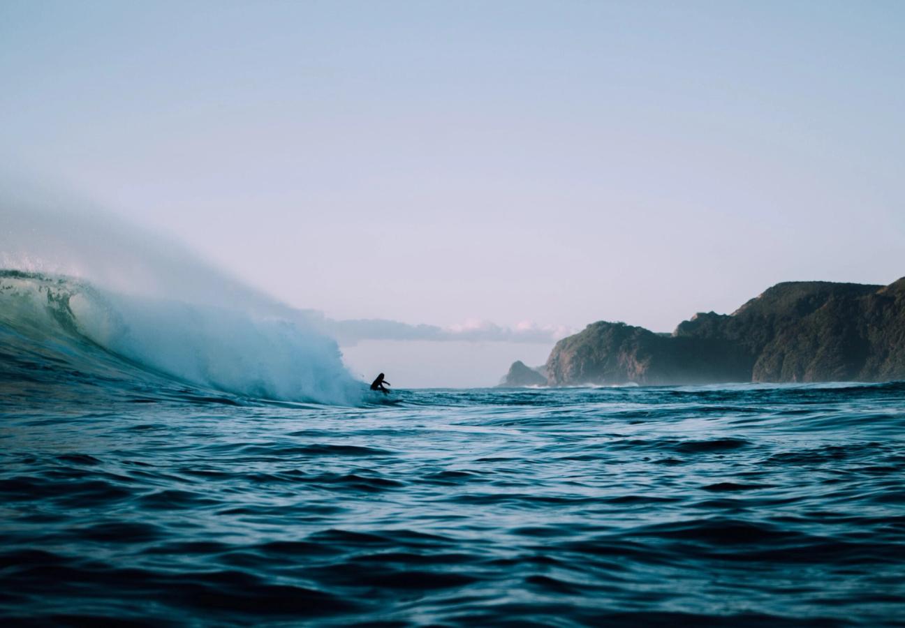 person surfs big wave off coast of beach in ocean