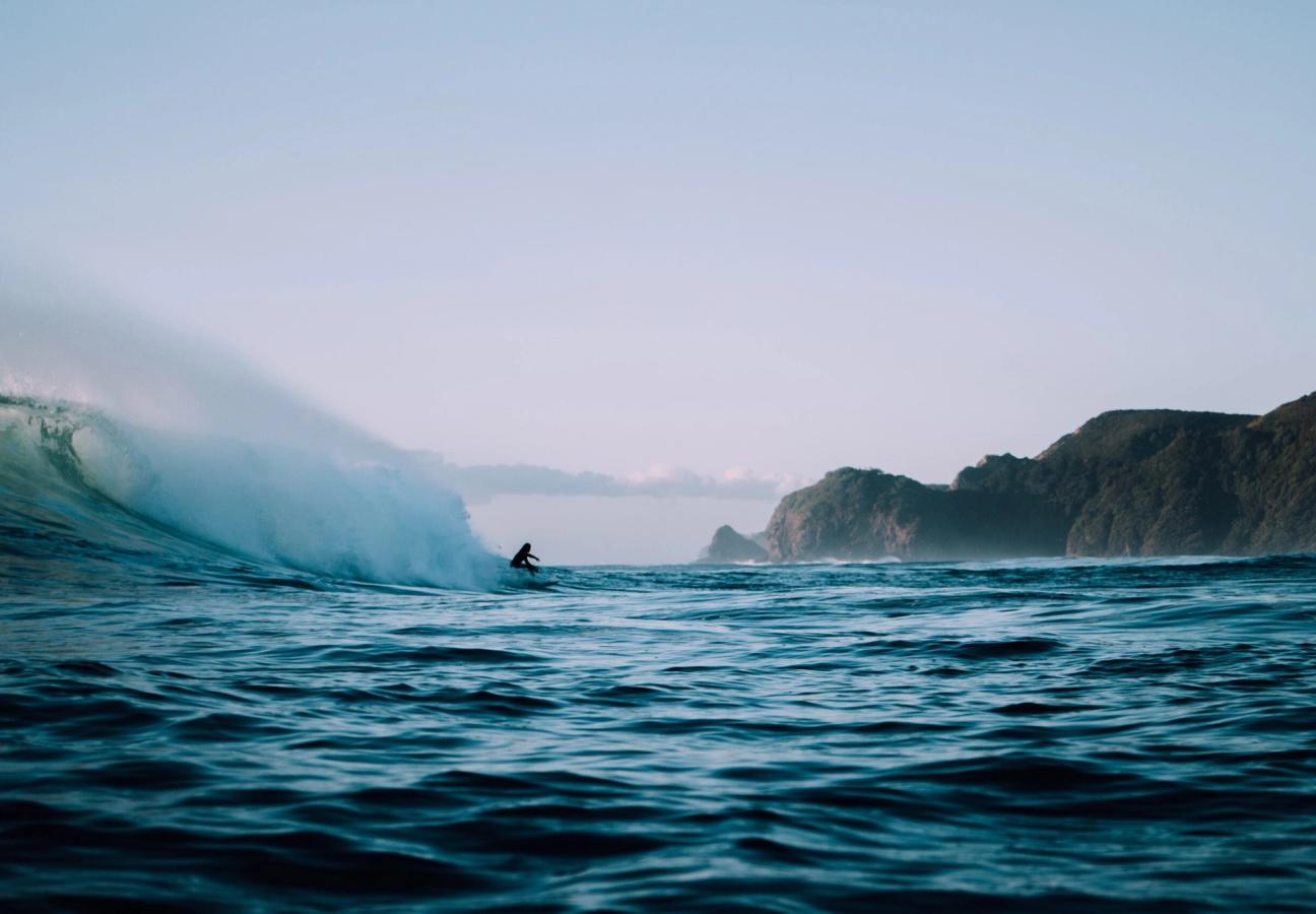 person surfs big wave off coast of beach in ocean