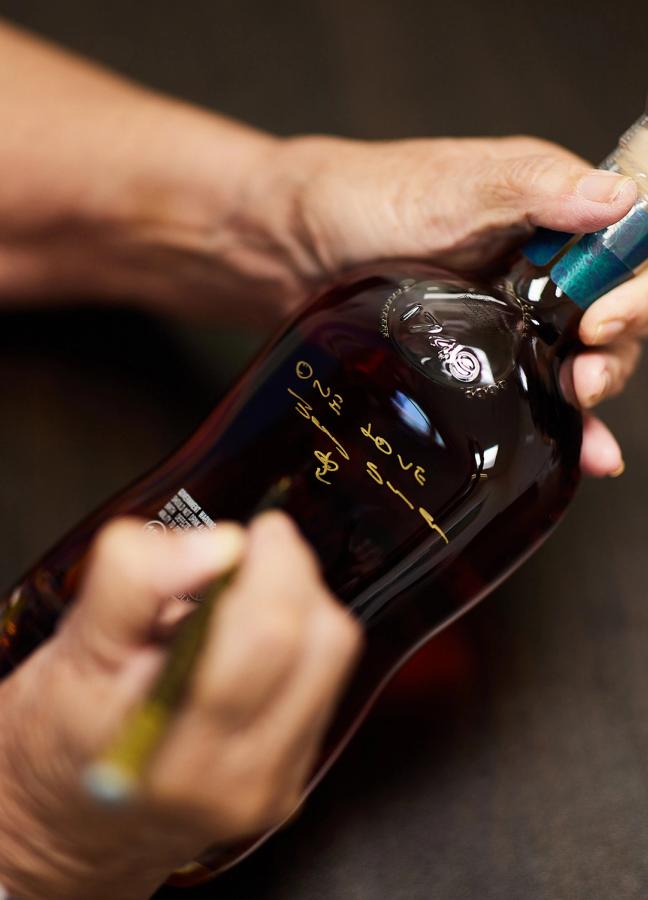 A person writing on an Appleton Estate rum bottle