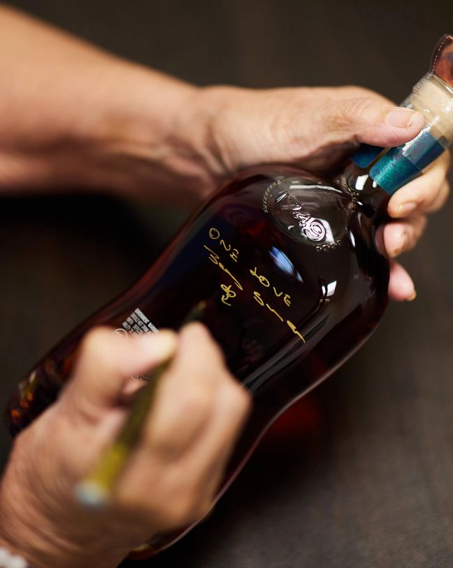 A person writing on an Appleton Estate rum bottle