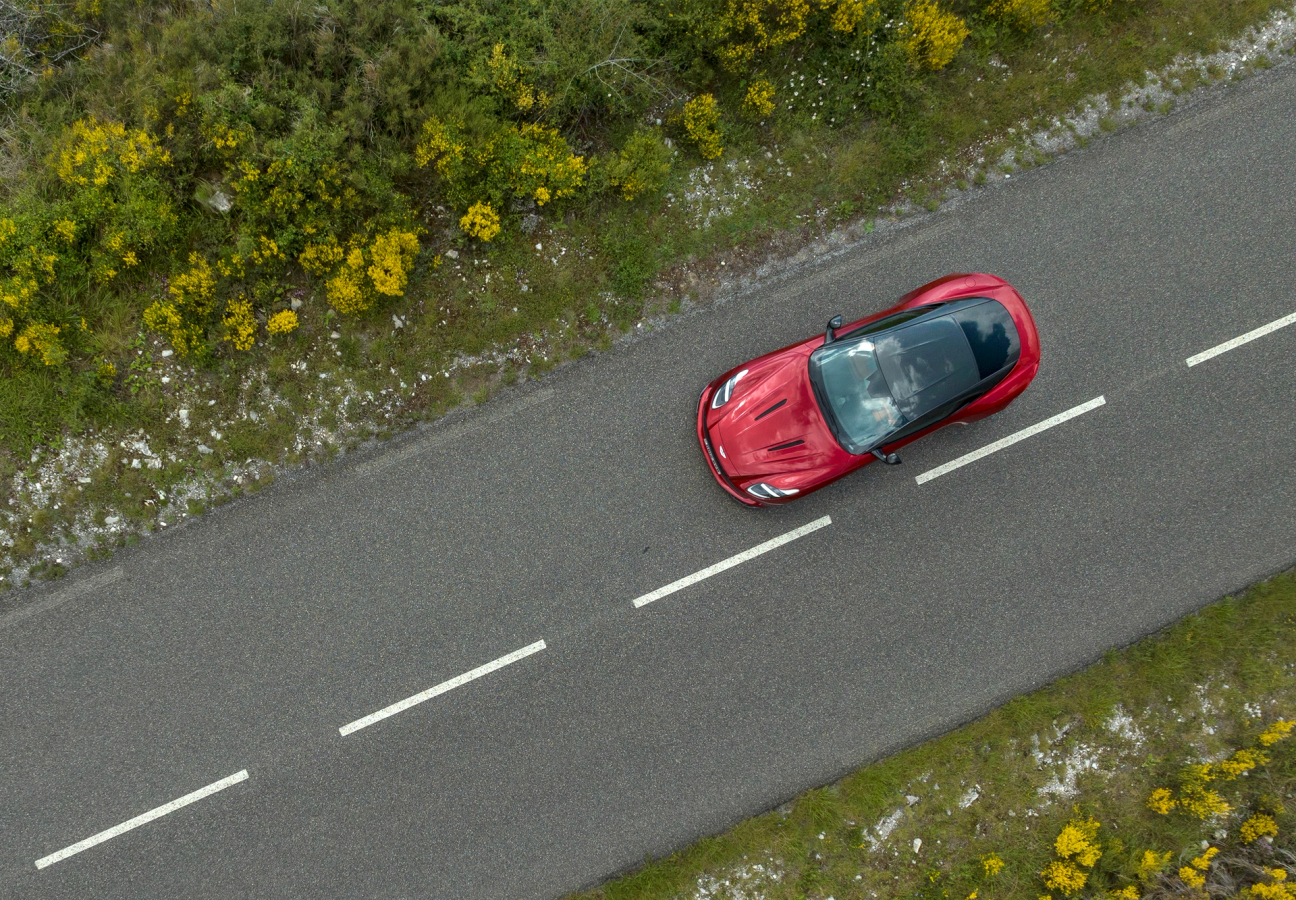 An aerial view of a red Aston Martin DB12 driving on the road