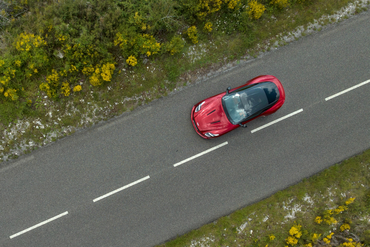 An aerial view of a red Aston Martin DB12 driving on the road