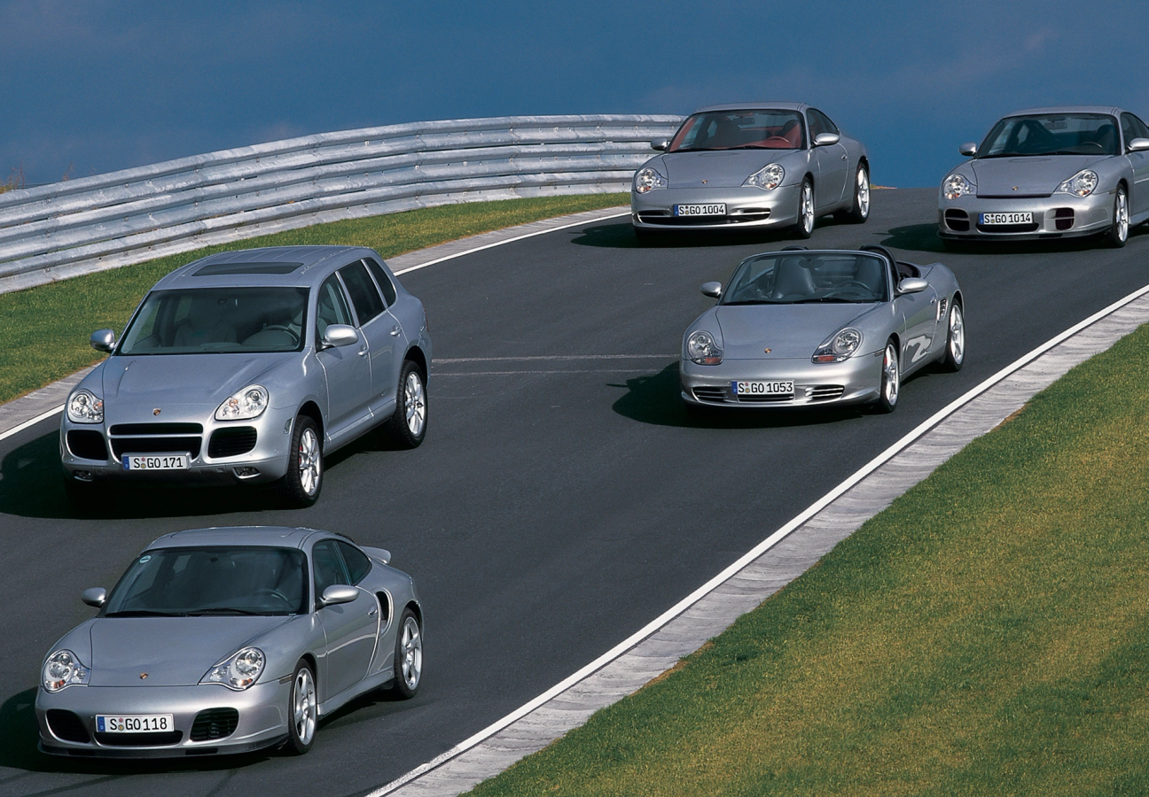 Multiple silver Porsche cars on a road from different decades