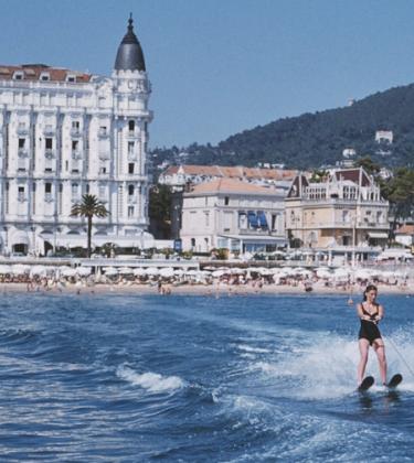 A Slim Aarons photo of two people jet-skiing outside the Carlton Cannes hotel front and beach club