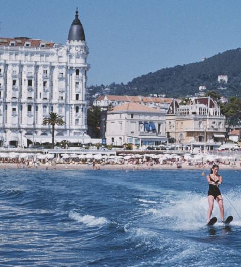 A Slim Aarons photo of two people jet-skiing outside the Carlton Cannes hotel front and beach club