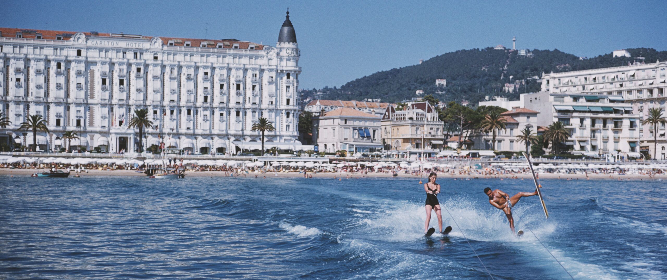 A Slim Aarons photo of two people jet-skiing outside the Carlton Cannes hotel front and beach club