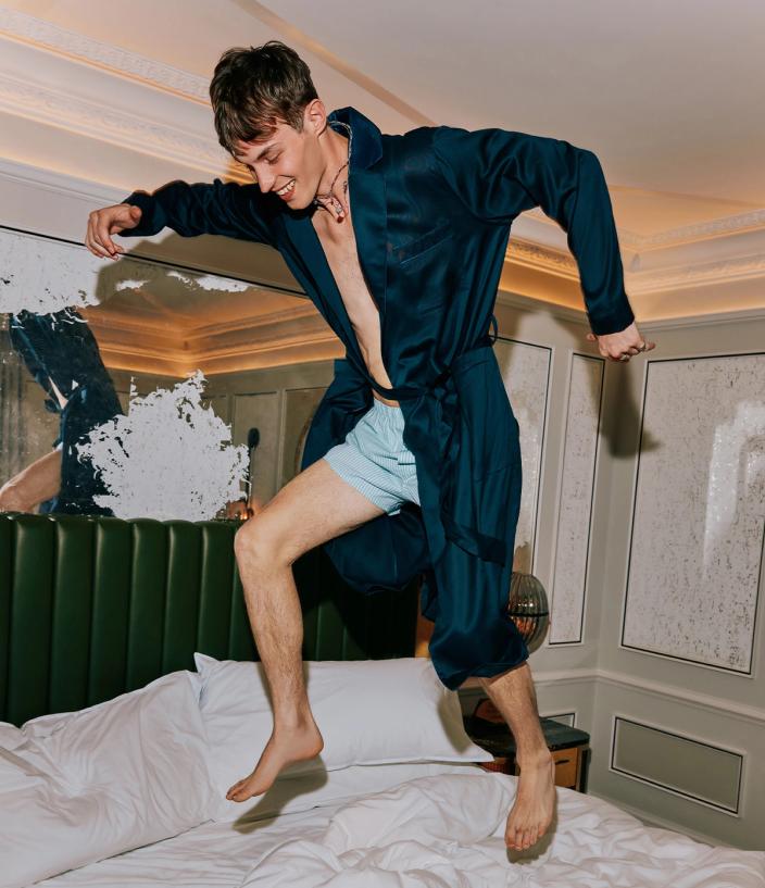 Model Kit Butler in a navy dressing gown jumping on a bed