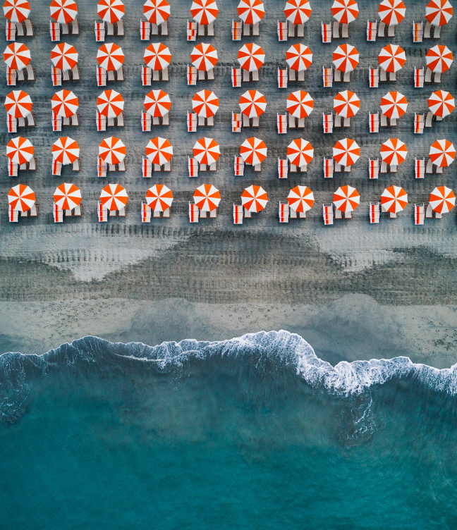 Ariel shot of beach filled with orange and white umbrellas in Massa Italy