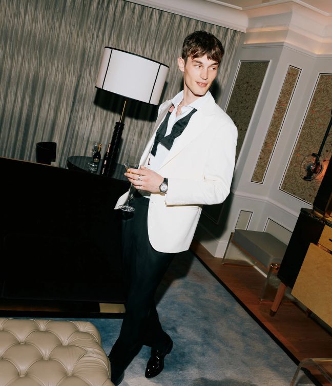 Model Kit Butler in a white tuxedo in a hotel room