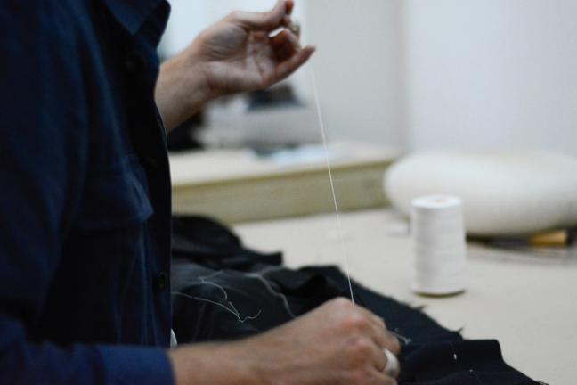 Tailor sewing together a suit with white thread
