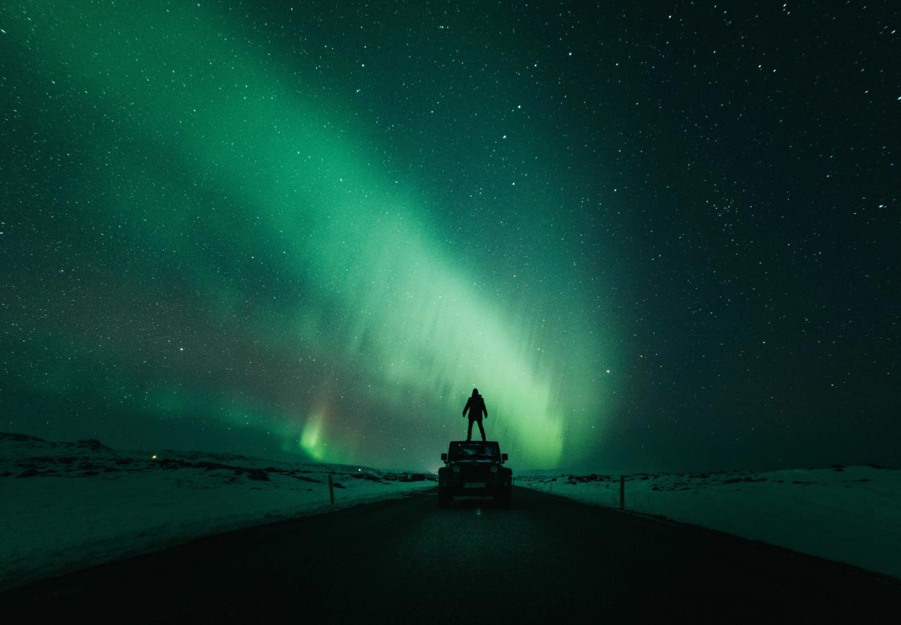 man stands on top of jeep while northern lights and stars are in the night sky above