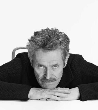 An image of actor Willem Dafoe wearing black and looking into the camera.