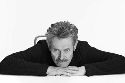 An image of actor Willem Dafoe wearing black and looking into the camera.