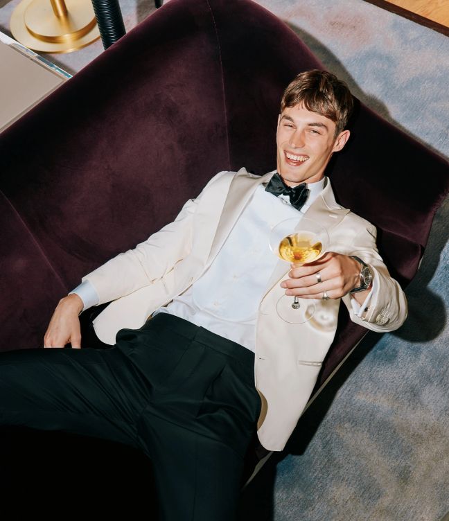 Model Kit Butler in a white tuxedo on a velvet sofa