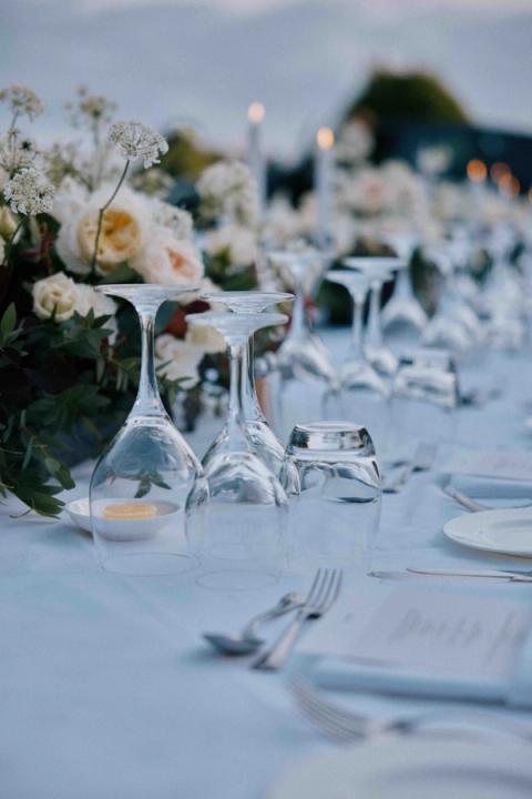 Set table with upside down wine glasses, set out cutlery and flower centerpiece