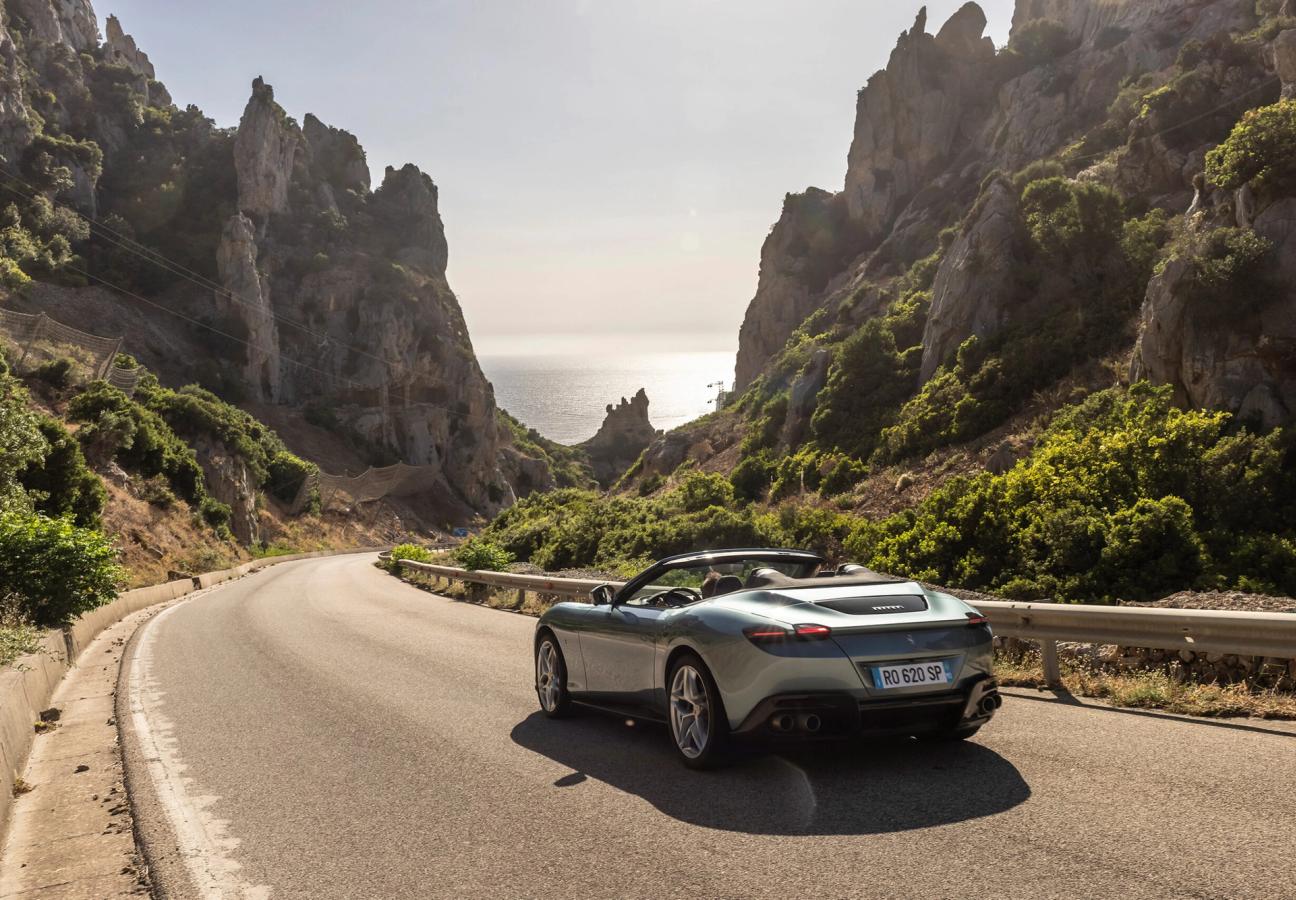 Ferrari Roma Spider driving along road between mountain range to the coast