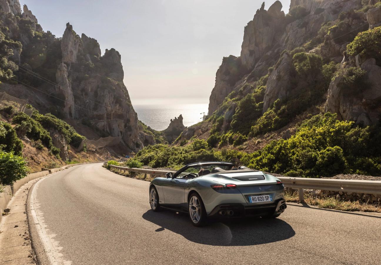 Ferrari Roma Spider driving along road between mountain range to the coast