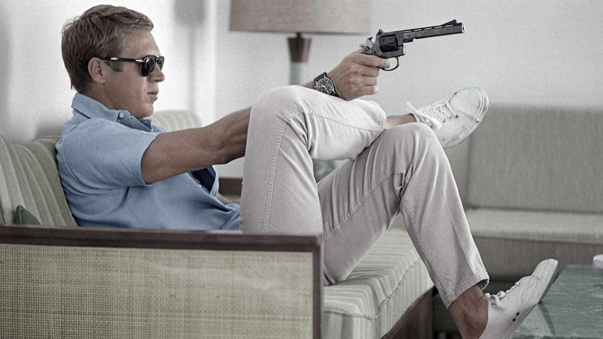 steve mcqueen wearing polo shirt and trainers pointing a gun