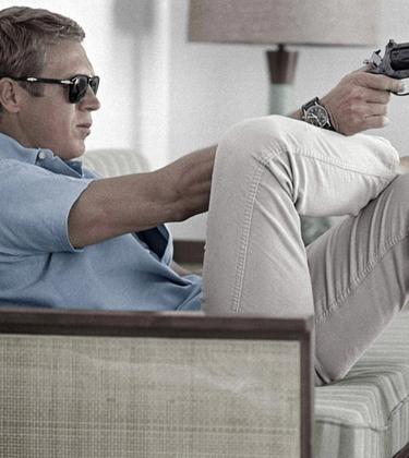 steve mcqueen wearing polo shirt and trainers pointing a gun