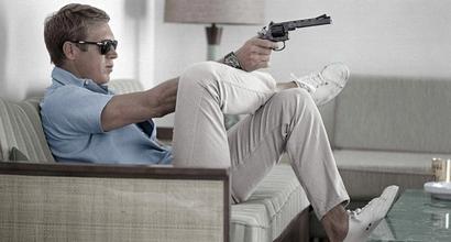 steve mcqueen wearing polo shirt and trainers pointing a gun
