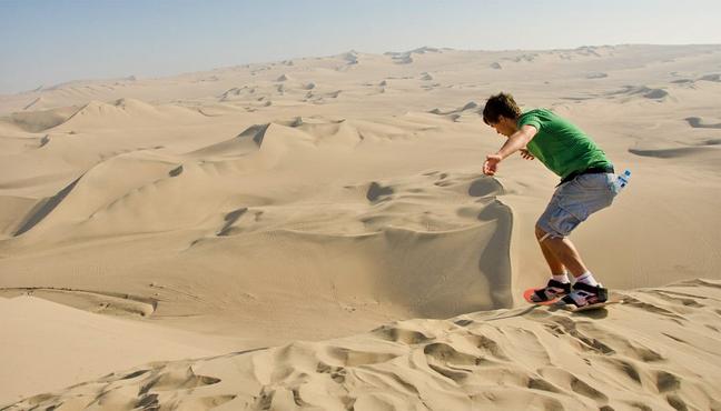 A man sand boarding over a desert dune in Peru