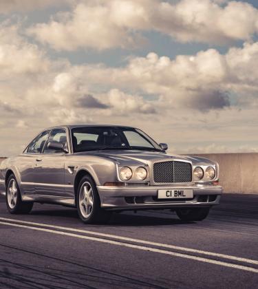 The original Bentley Continental GT driving on a road with blue cloudy sky behind